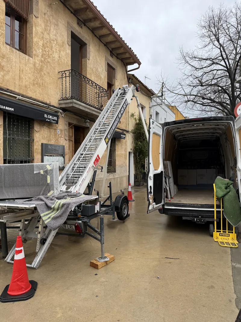 Elevador de mudanzas y furgoneta trabajando en una calle estrecha